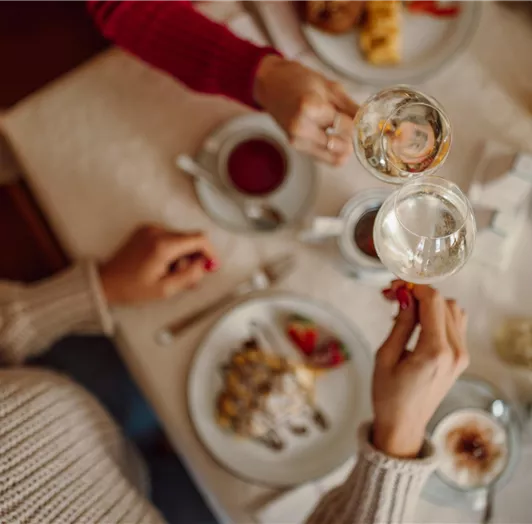 Sparkling wine for breakfast: A table with delicious food and drinks. Two people clink glasses.