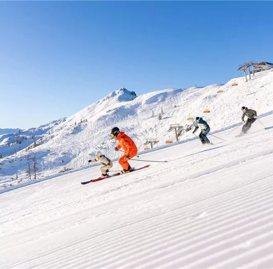 Skifahrer fahren in einer wunderschönen, schneebedeckten Landschaft. Der Himmel ist klar und blau, umgeben von Bergen.