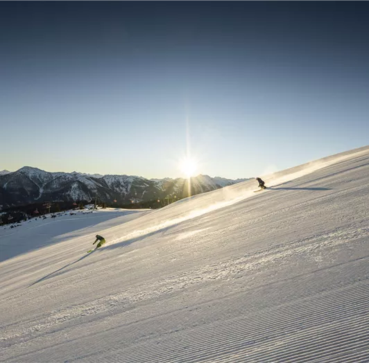 Erste Abfahrt um 8:00 Uhr im Snow Space Salzburg. Im Hintergrund leuchtet die Sonne über den Bergen.