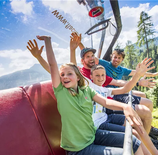 Eine fröhliche Gruppe von vier Personen fährt in einer Gondel in die Berge.