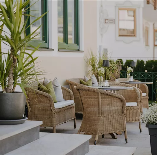 Eine elegante Sonnenterrasse mit gemütlichen Rattanmöbeln und grünen Pflanzen. Die Atmosphäre ist einladend und entspannend.