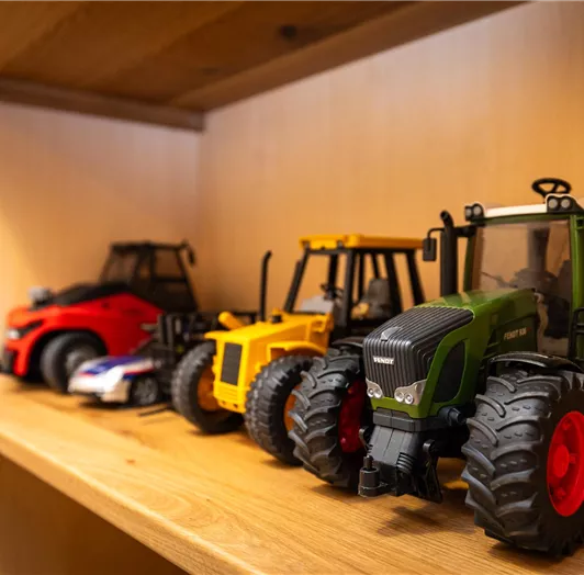 Eine Reihe von Spielzeugtraktoren in verschiedenen Farben steht auf einem Holzregal. Die Modelle sind detailliert und zeigen die Vielfalt landwirtschaftlicher Fahrzeuge.