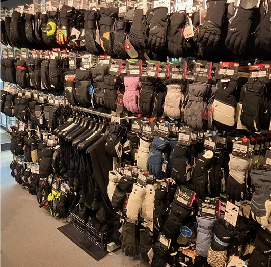Eine große Auswahl an Handschuhen hängt an einem Verkaufsregal. Die Handschuhe sind in verschiedenen Stilen und Farben angeordnet.