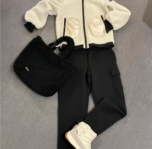 Eine modische Winter-Outfit-Kombination mit einer weißen Jacke, schwarzer Hose, bequemen Stiefeln und einer schwarzen Tasche.