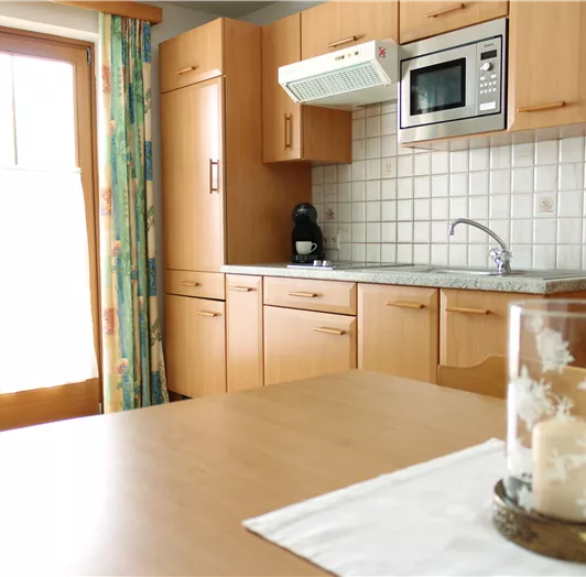 Eine moderne Küche mit Holzmöbeln und hellen Fliesen. Auf dem Tisch steht eine dekorative Kerze in einem Glas.