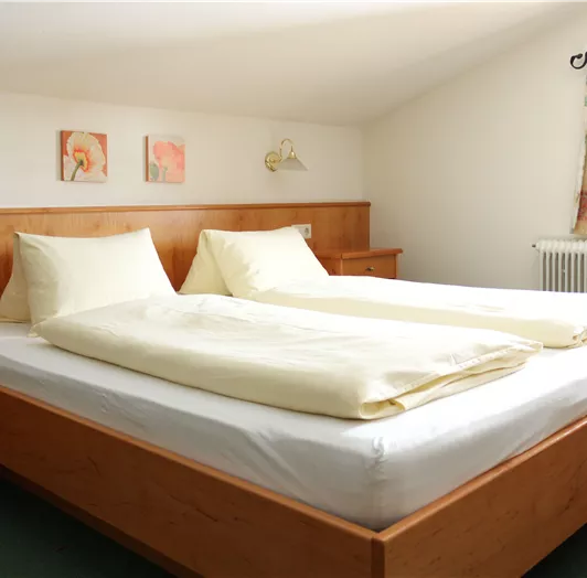 Ein helles und gemütliches Schlafzimmer mit einem großen Doppelbett. Die Wände sind geschmückt mit zwei Kunstwerken und es gibt einen schönen Blick nach draußen.