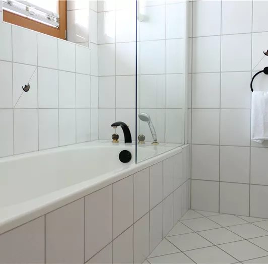Ein modernes Badezimmer mit einer Badewanne und Glasduschabtrennung. Die Wände sind mit weißen Fliesen gefliest und es gibt ein Handtuchhalter.