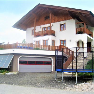 Ein schönes Haus mit Balkon und großer Terrasse. Im Garten befindet sich ein Trampolin.