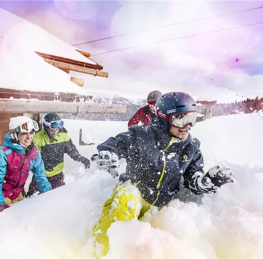 Eine Gruppe von Freunden genießt den Spaß im frischen Schnee. Sie tragen Skiausrüstung und lachen, während sie im Schnee spielen.
