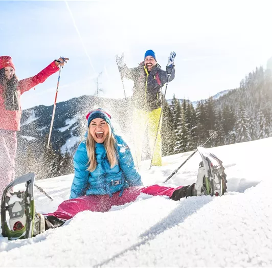 Drei fröhliche Menschen genießen den Schnee bei einer Schneeschuhwanderung.